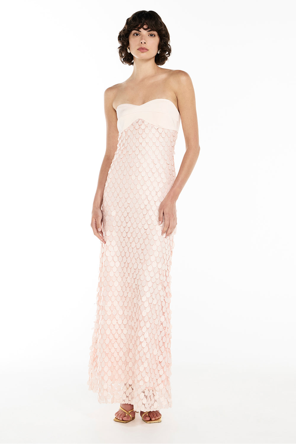 A model wearing a pink strapless maxi dress with a crepe satin bodice and teardrop lace applique on the skirt.