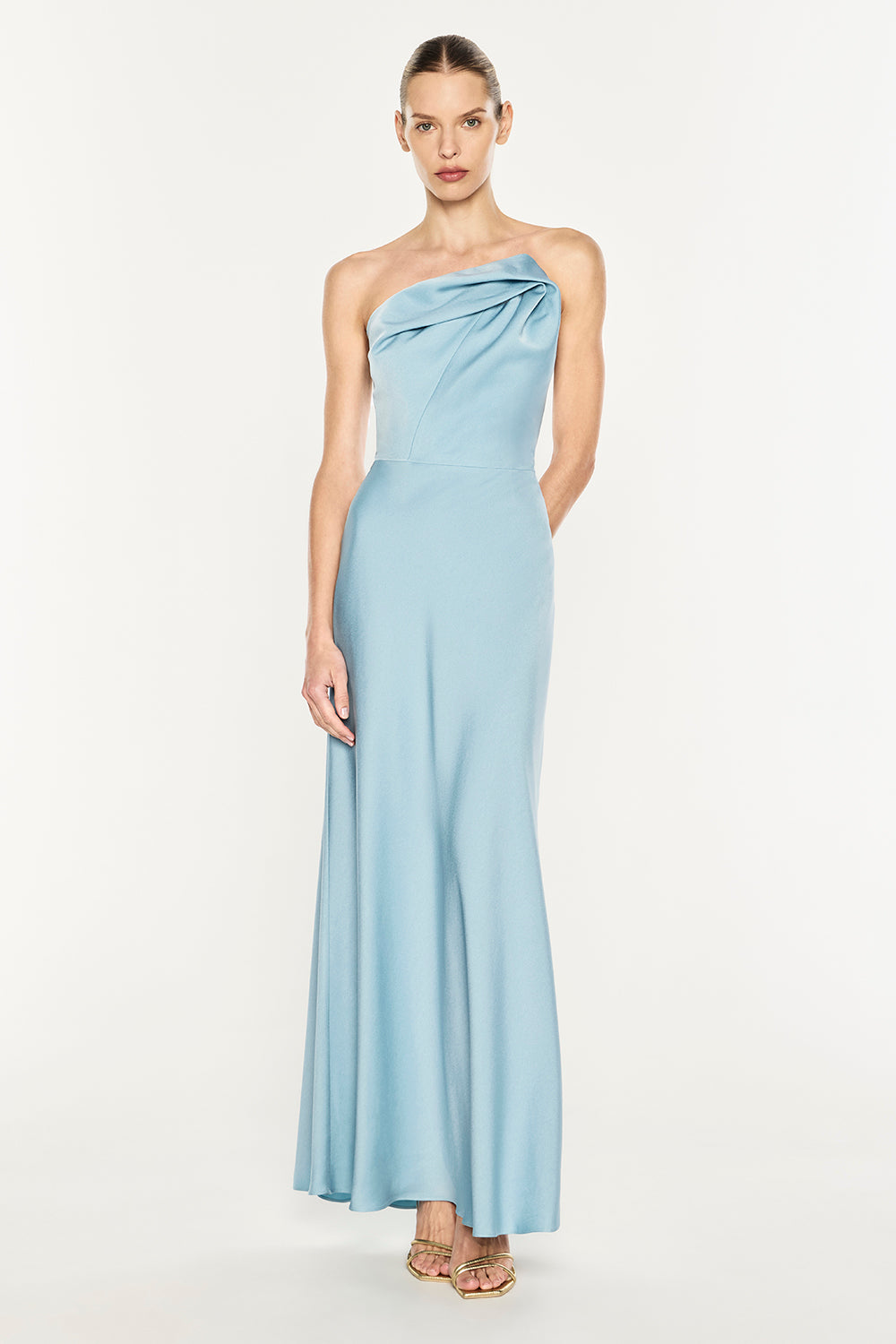 A woman modeling a light blue one-shoulder satin maxi dress against a plain white studio background.